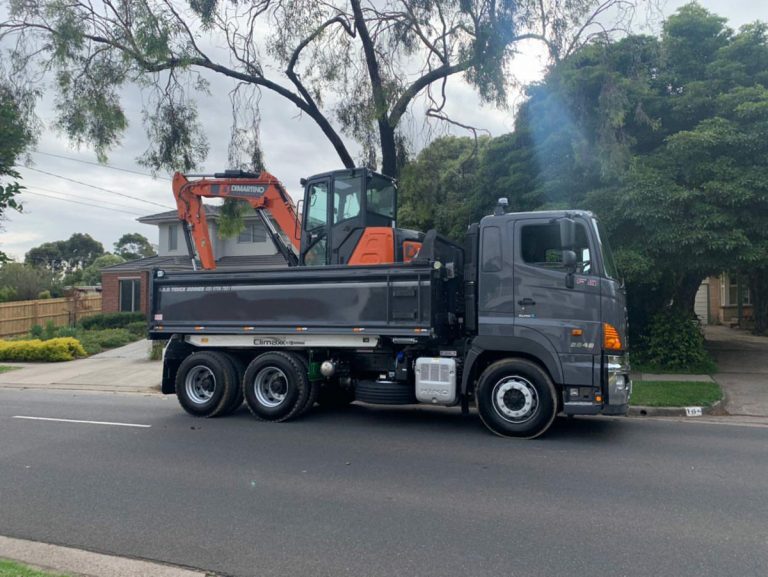 Grey Hino truck with custom tipper truck body with custom grey paint finish carrying a digger